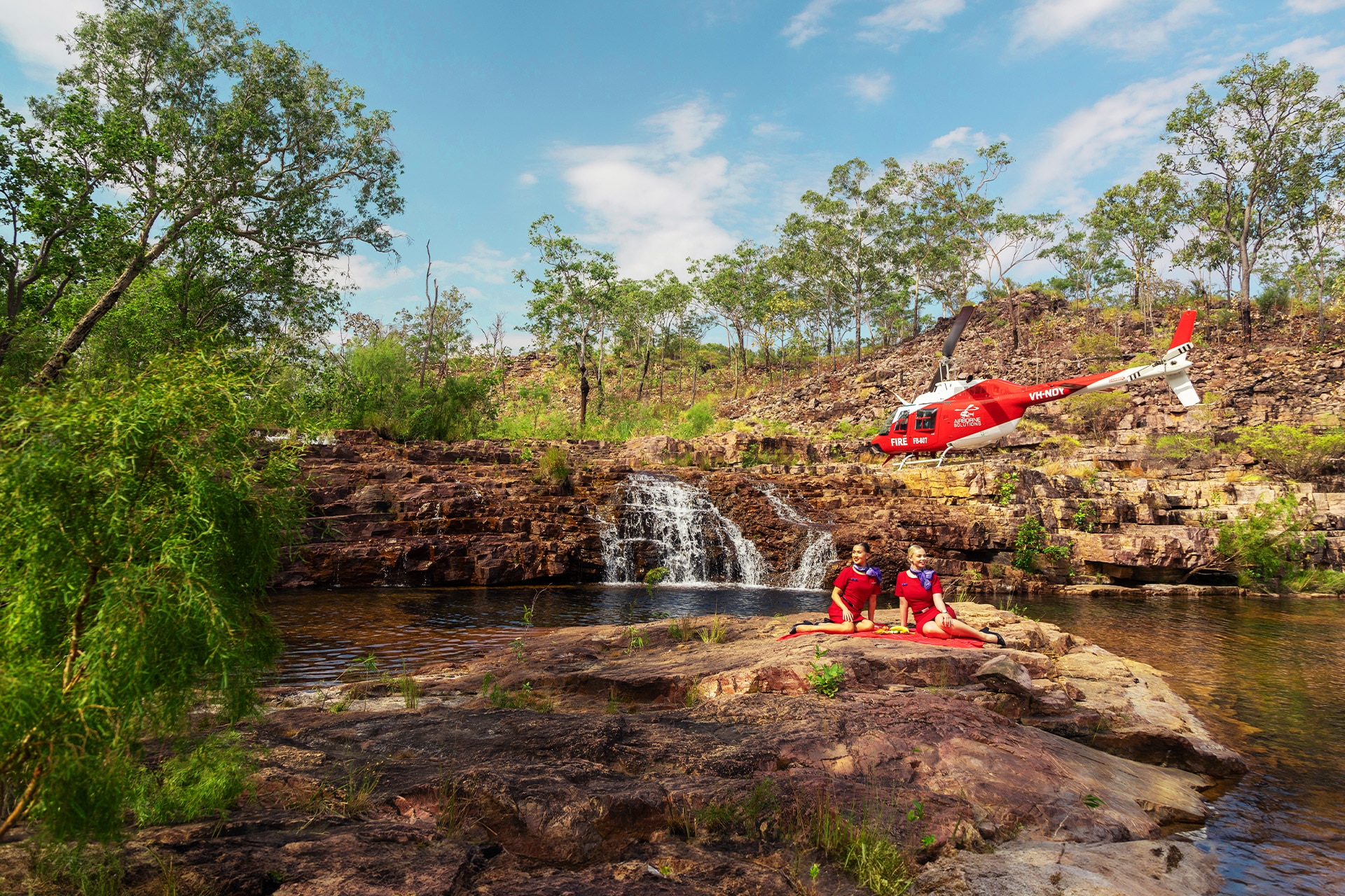 Two flight attendants laying on a rock as a helicopter flies past in the Northern Territory