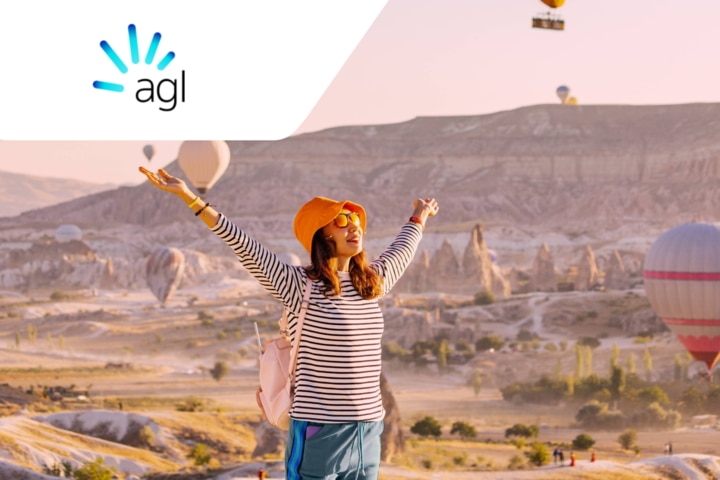 A person with her arms raised in the air with hot air balloons in the background